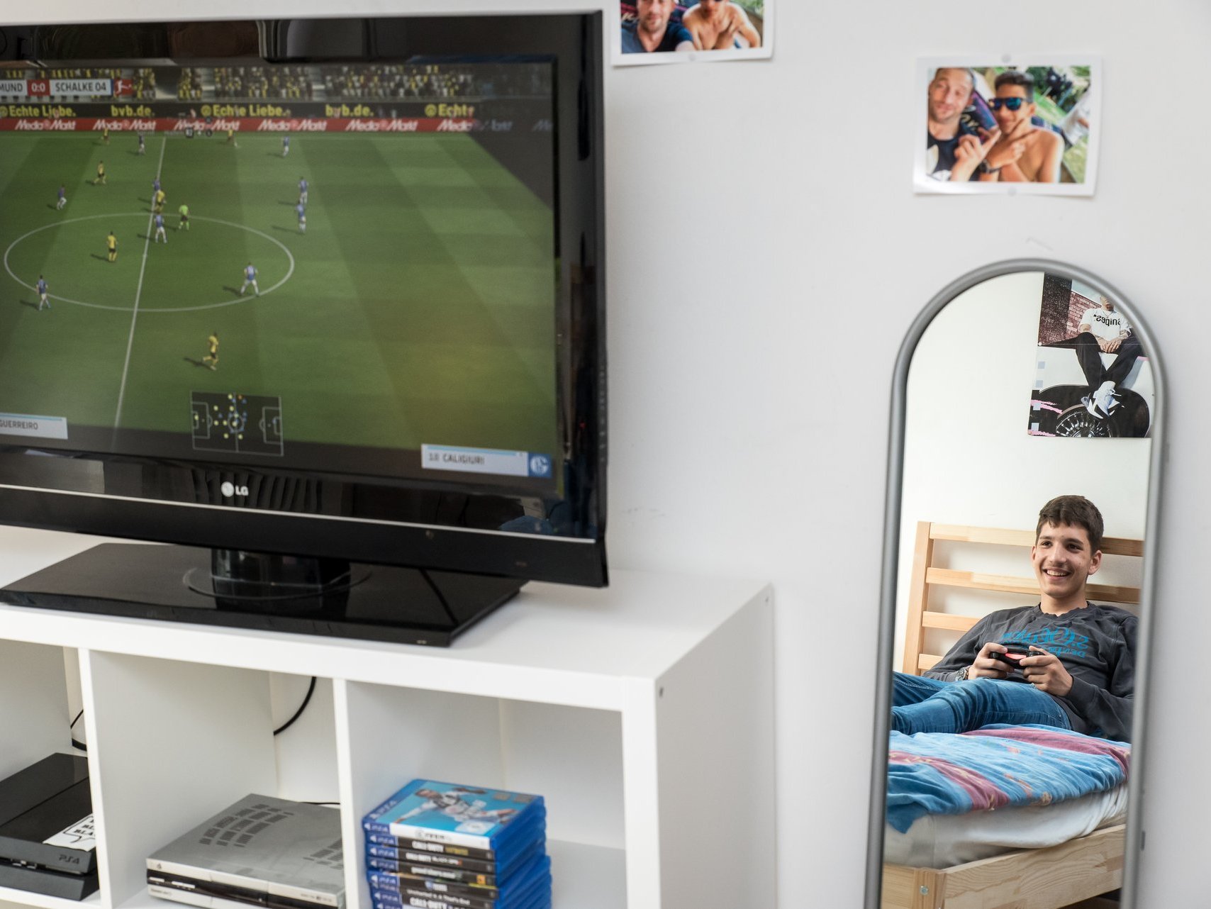 Bildperspektive zeigt gleichzeitig den TV mit Computer-Fussballspiel und im Spiegel daneben ist der Junge zu sehen, der den Controller hält