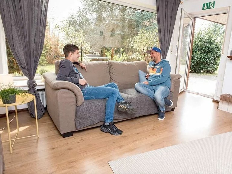 zwei junge Männer unterhalten sich auf einem Sofa, lachend 