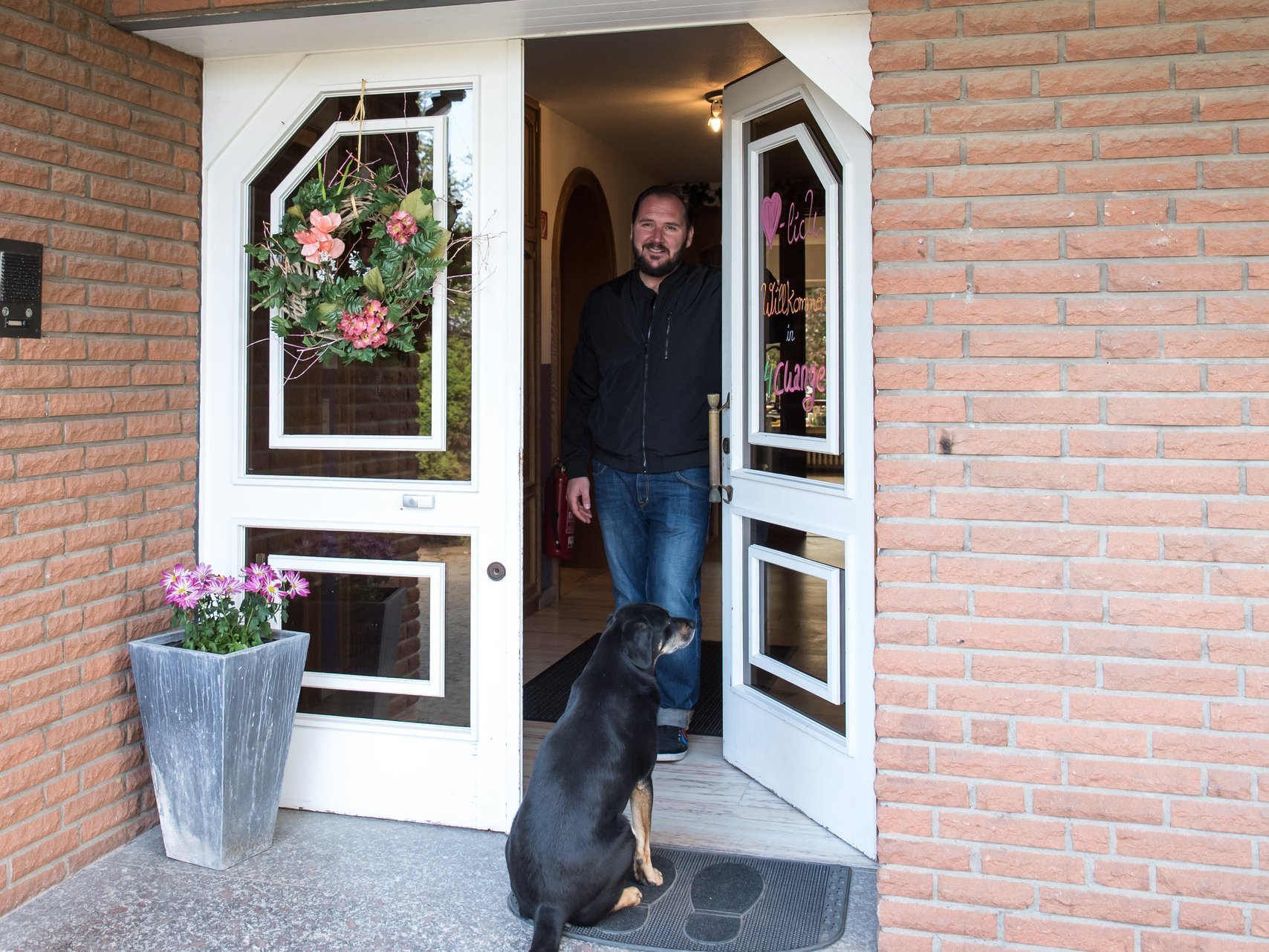 Junger mann mit Bart steht in geöffneter Haustür und lächelt in die Kamera