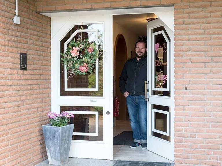 junger Mann mit Bart steht in geöffneter Haustüre und lächelt in die Kamera